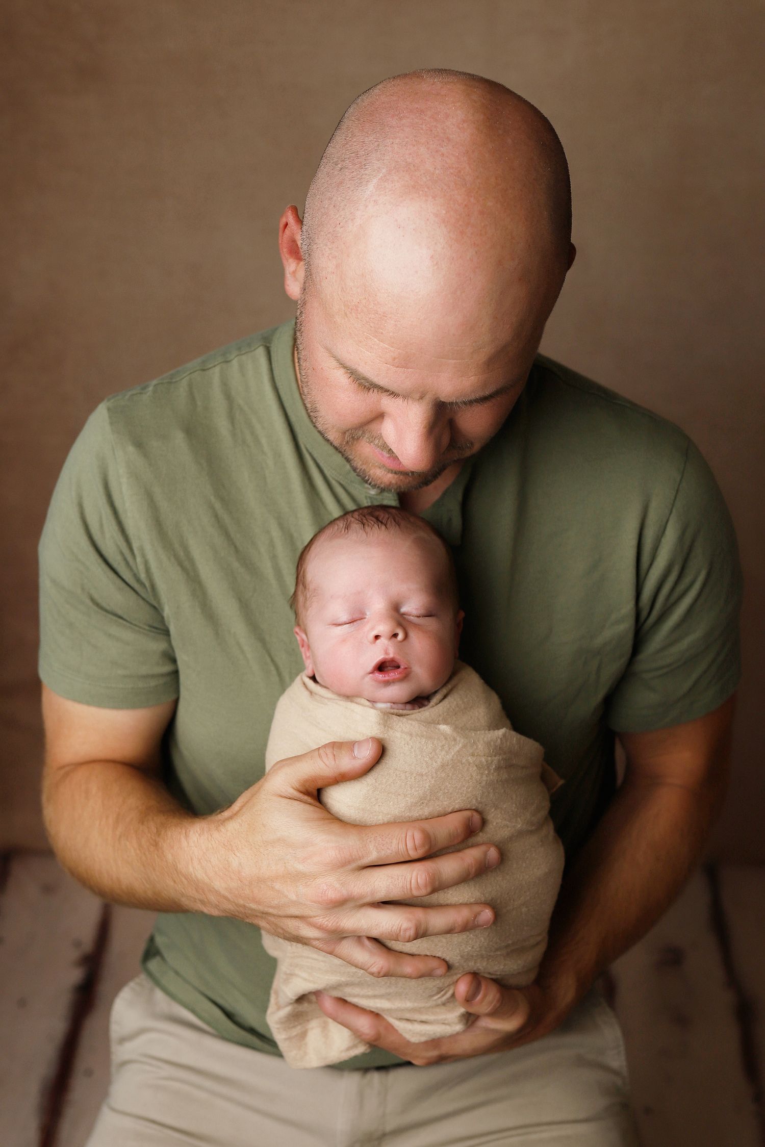 A person wearing a green t-shirt holds and gazes lovingly at a swaddled newborn in a series of connected images.