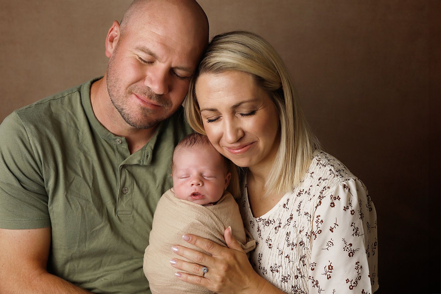 Peaceful portrait of loving parents holding their sleeping newborn baby in natural warm tones.