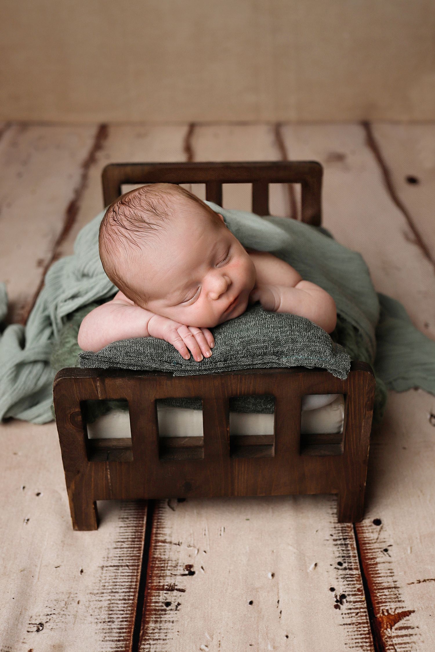 Baby peacefully sleeping on rustic wooden bench in sage green swaddle blanket.