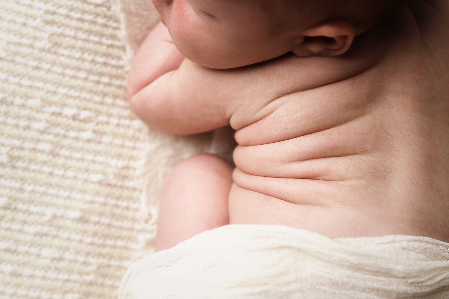 Close up of a newborn baby's delicate skin folds against a soft white blanket backdrop. Utah newborn photography