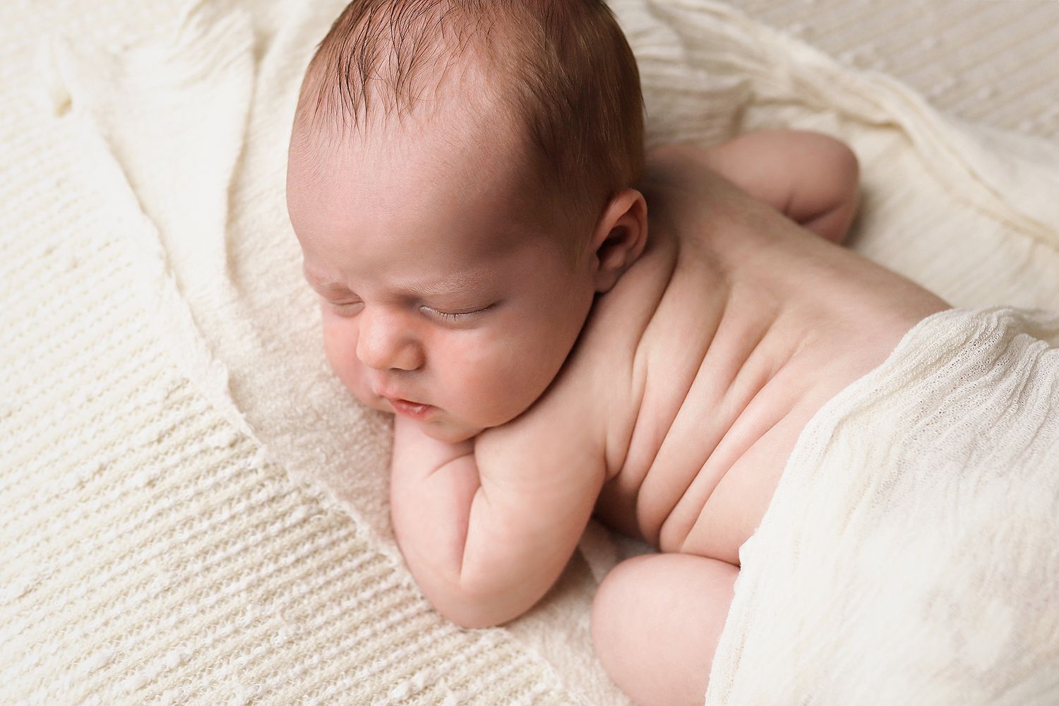 Peaceful sleeping newborn baby lying on soft white textured blanket in natural light. West Jordan newborn photography