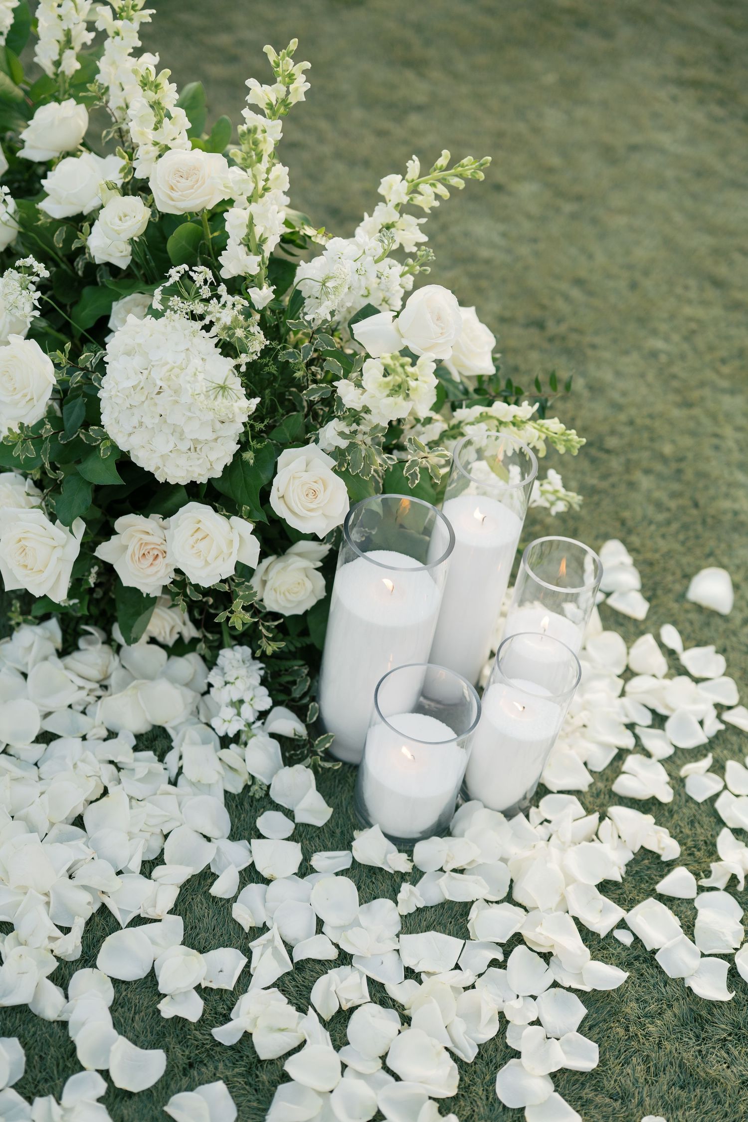 White floral arrangements with roses and hydrangeas surrounded by glowing candles create an elegant wedding table display.