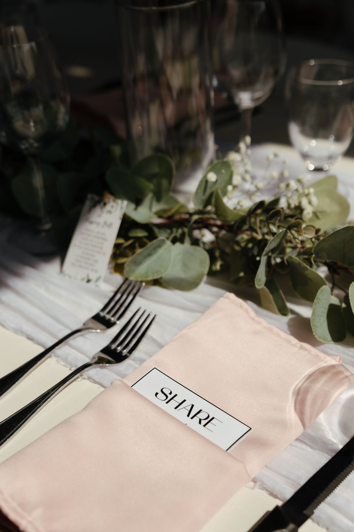 Elegant table setting with white napkins, black cutlery, and eucalyptus leaves creating a modern wedding reception design.