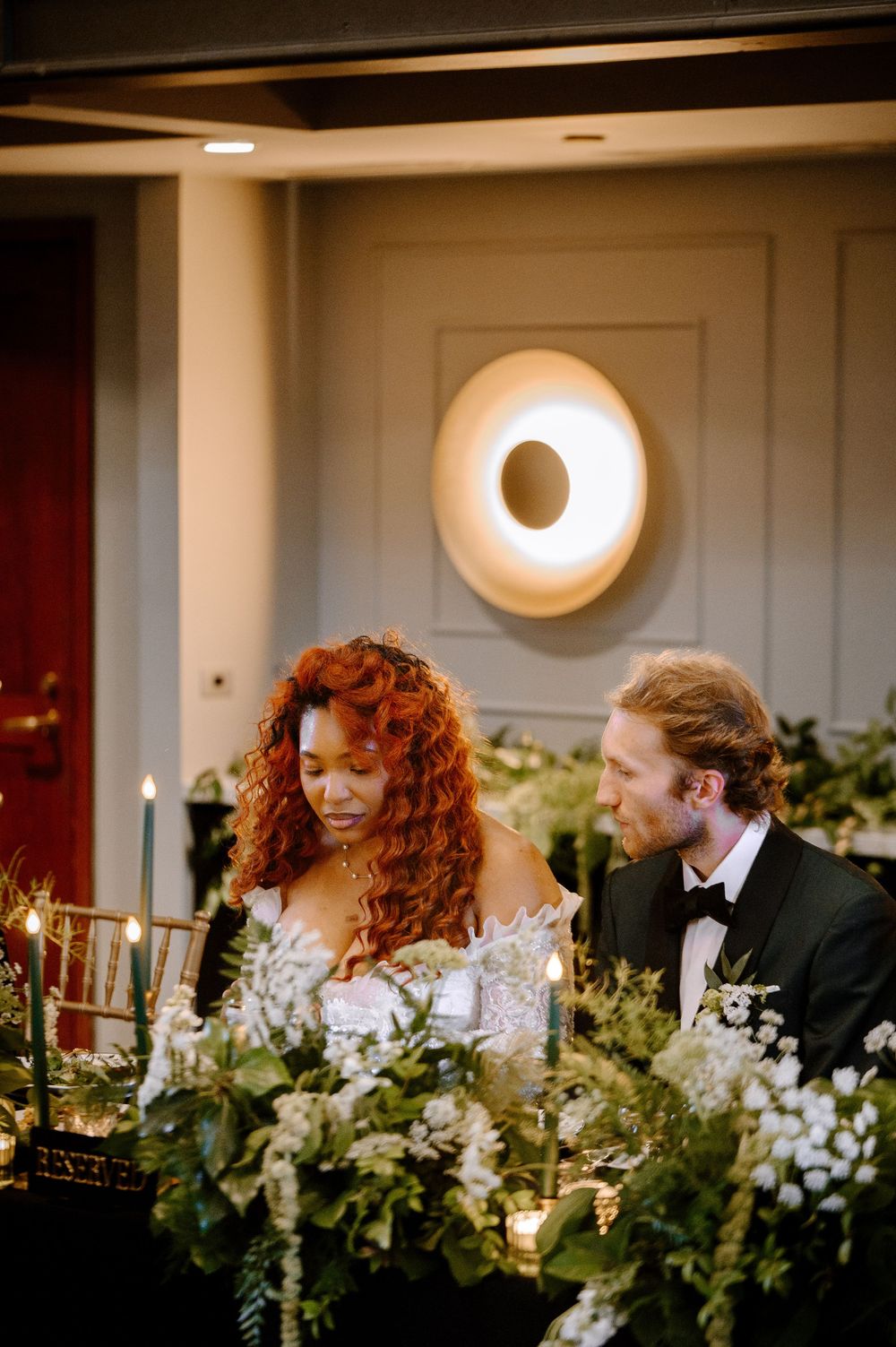 Reception decor features romantic candlelit greenery garlands with white flowers at an elegant evening wedding celebration.