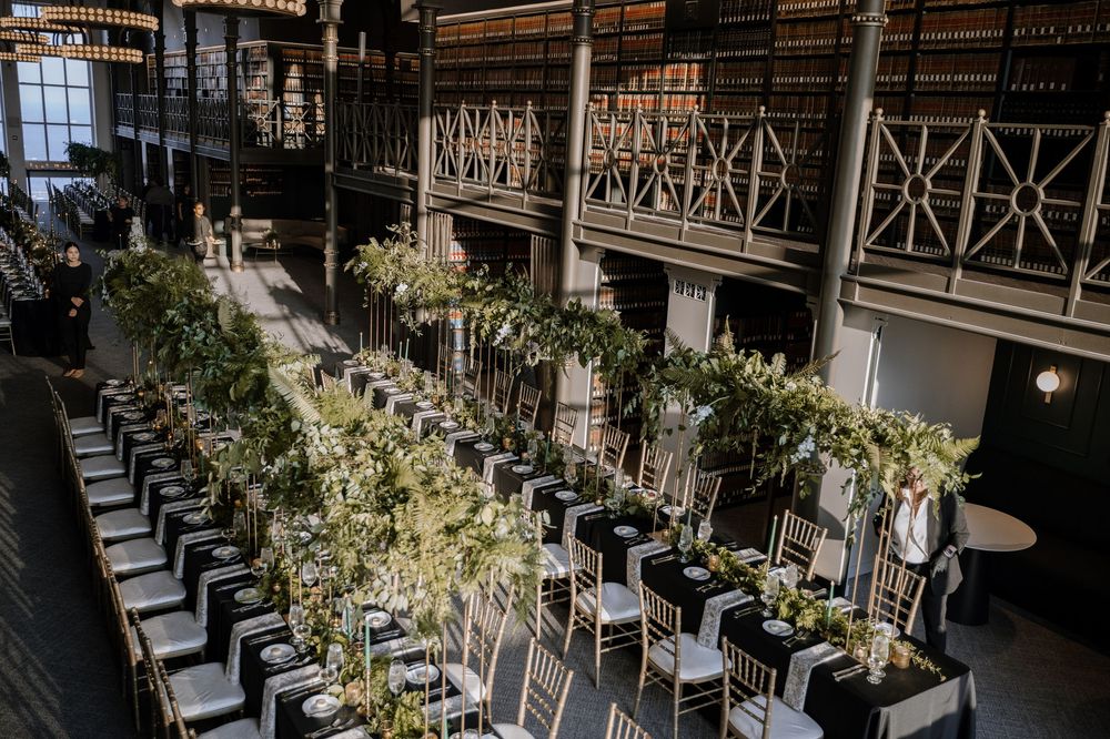 Long banquet tables with elegant floral arrangements line an industrial-style venue with exposed beams and railings.