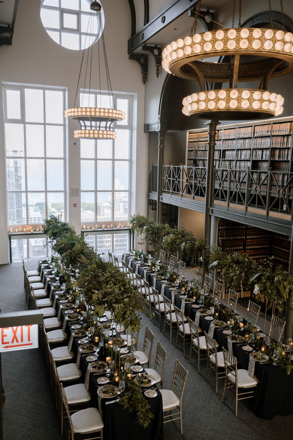 Elegant wedding reception venue with circular chandeliers, long dining tables, and lush greenery decorations.