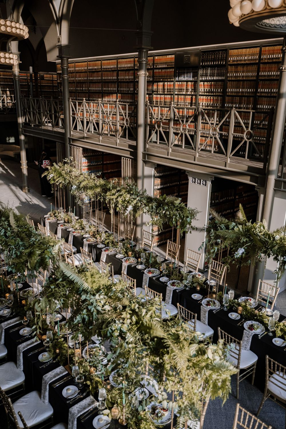 Elegant wedding reception tables decorated with lush greenery and white floral arrangements in a grand ballroom venue.
