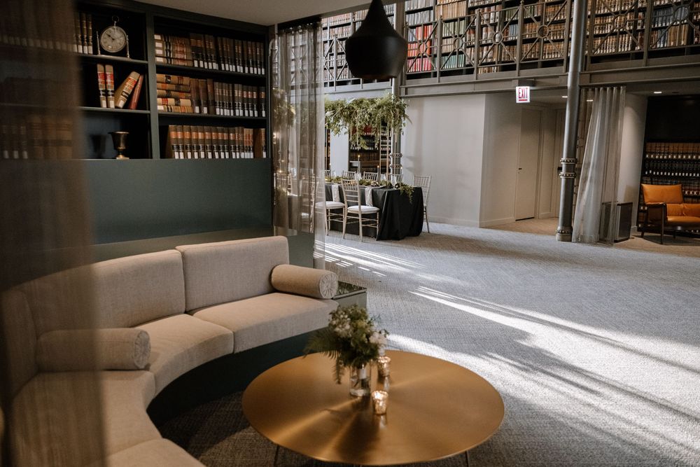 A library interior with floor to ceiling bookshelves, natural light streaming through windows, and lounge seating areas.