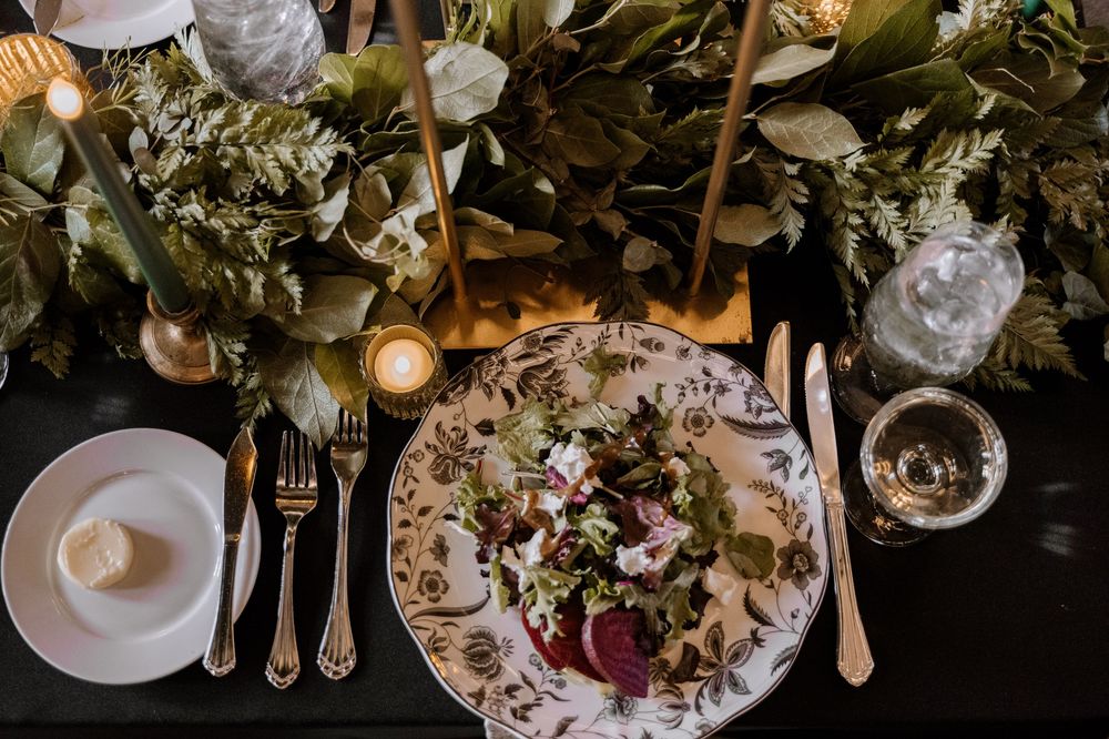 Overhead view of an elegant table setting with wine glasses, candles and floral arrangements adorned with pink roses and greenery.