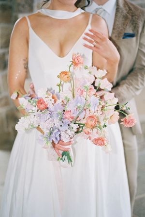 A row of bridesmaids holding delicate pink and lavender floral bouquets against white dresses.