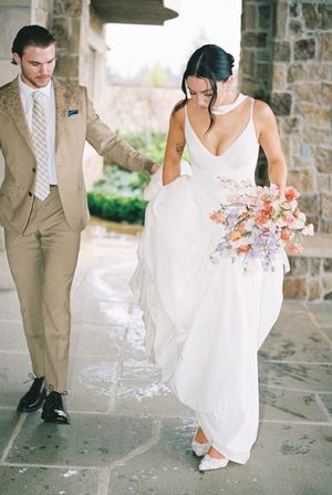 A wedding couple walking on stone pavement, with the bride holding a pink and coral floral bouquet.