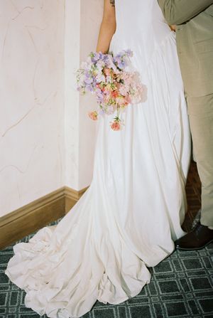 A flowing white wedding dress with a delicate pink and purple bouquet trailing along the floor.