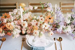 Elegant table setting with peach and lavender floral centerpiece arrangement alongside gold cutlery and white plates.