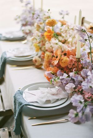 Elegant table setting with lavender and peach floral arrangements, white plates, and candles for a wedding reception.