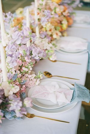 Wedding reception table decorated with delicate pink and purple flowers along white place settings.