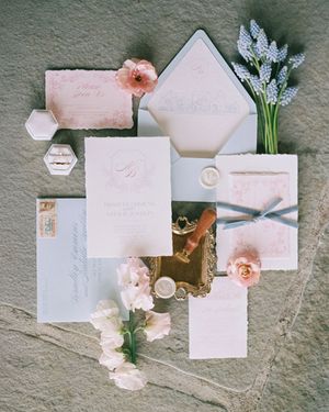 Elegant wedding stationery suite with blush pink envelopes and delicate floral accents on gray surface.