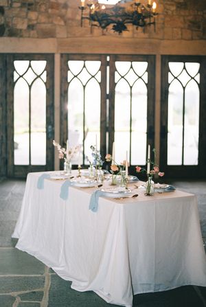 Elegant white dining tables set up in a stone castle room with gothic arched windows and chandeliers.