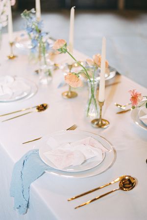 Romantic table setting with gold cutlery, pastel flowers, and soft candlelight for an elegant reception.