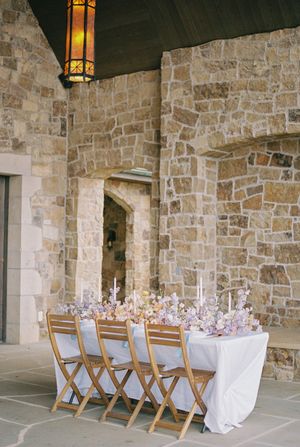 A rustic stone wall reception area with wooden folding chairs and white tablecloths under warm lighting.