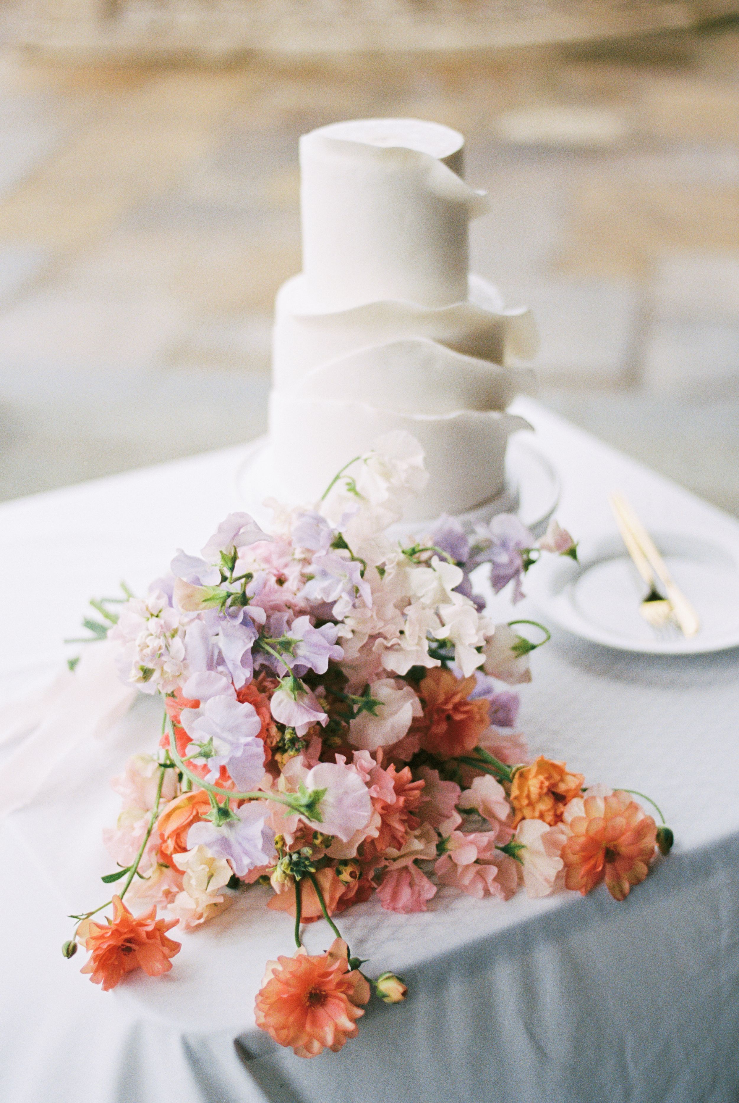 Delicate pink and coral floral arrangements adorning a white wedding cake on an elegant table setting.