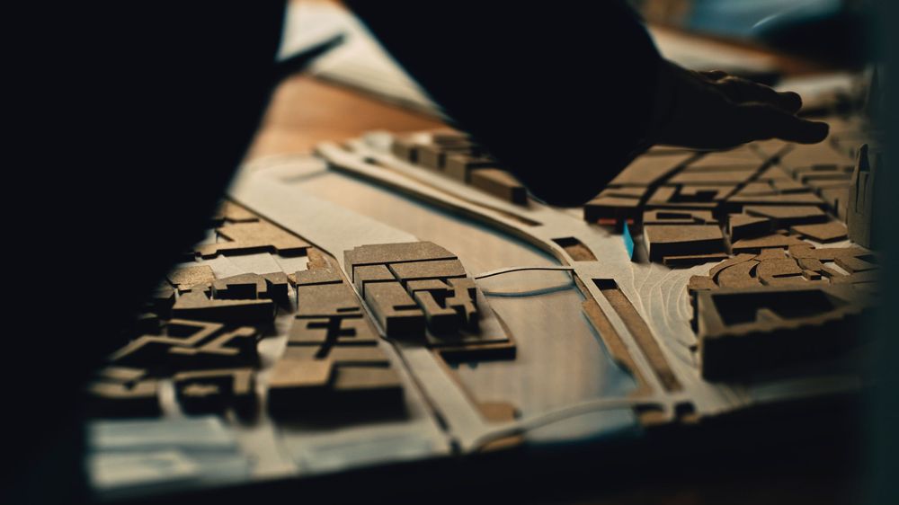 Person working on a complex wooden puzzle or assembly project at a wooden table in dramatic lighting.