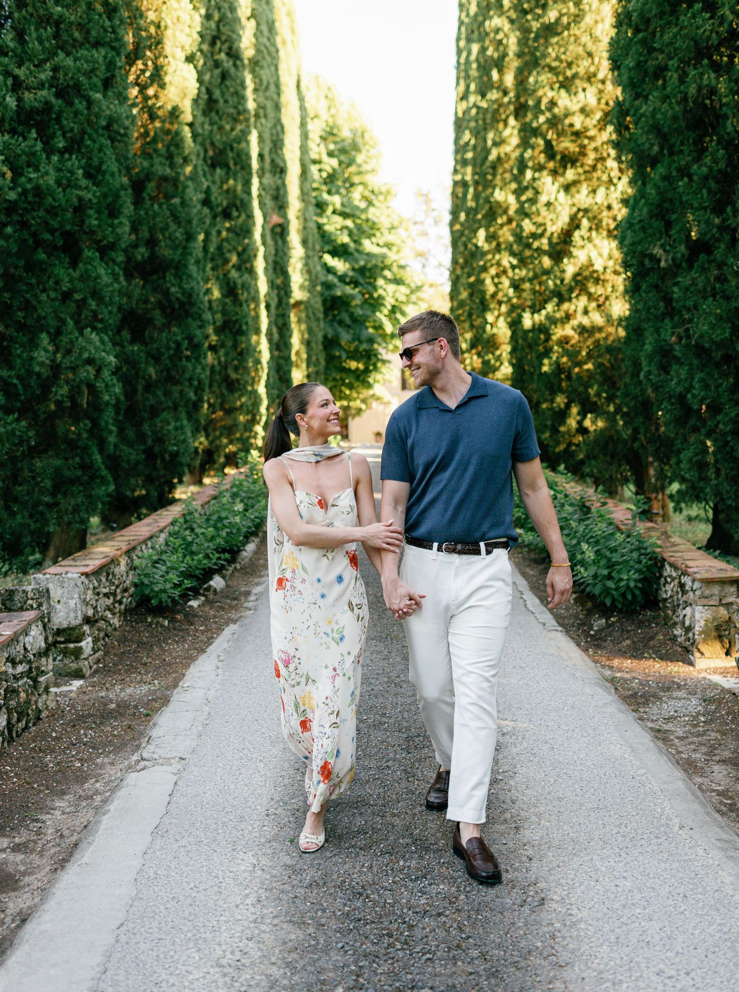 A couple walking and dancing together on a tree-lined gravel path during a romantic sunset moment at at Borgo San Luigi.