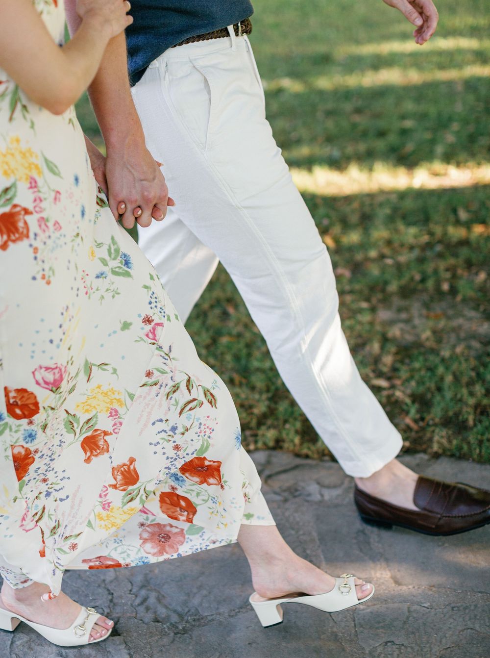 Person wearing white pants and floral dress walks on stone path showing unique blend of formal and casual wedding attire.