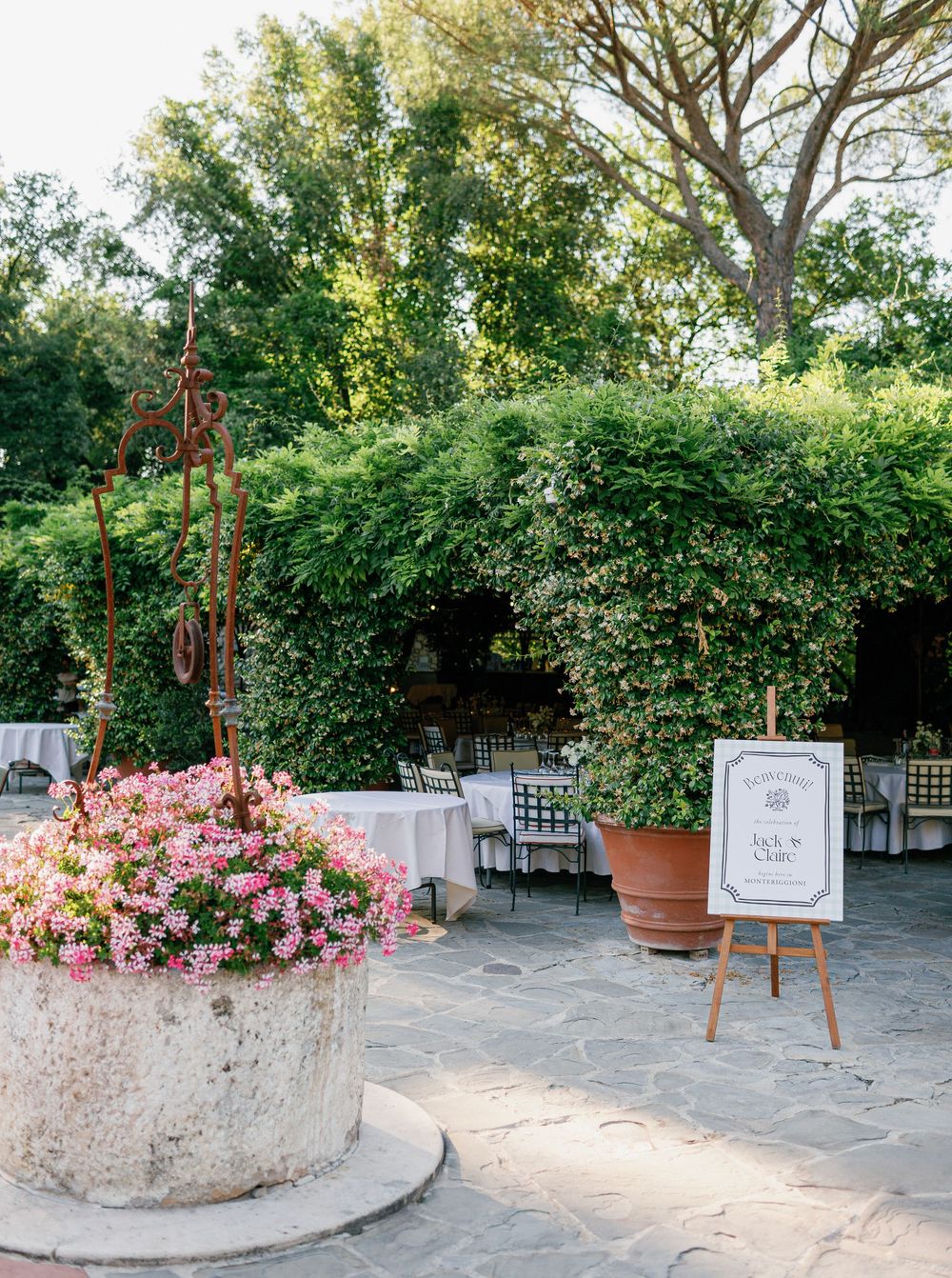 Elegant outdoor at Borgo San Luigi wedding venue setup with pink floral arrangements in stone planters and decorative easel displays.