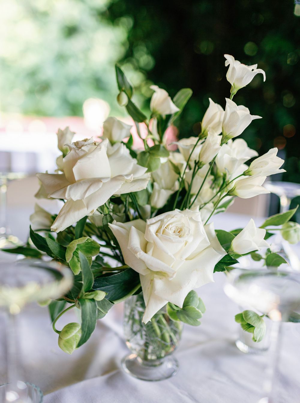 Several elegant white roses with greenery arranged in glass vases create a minimalist wedding table centerpiece.