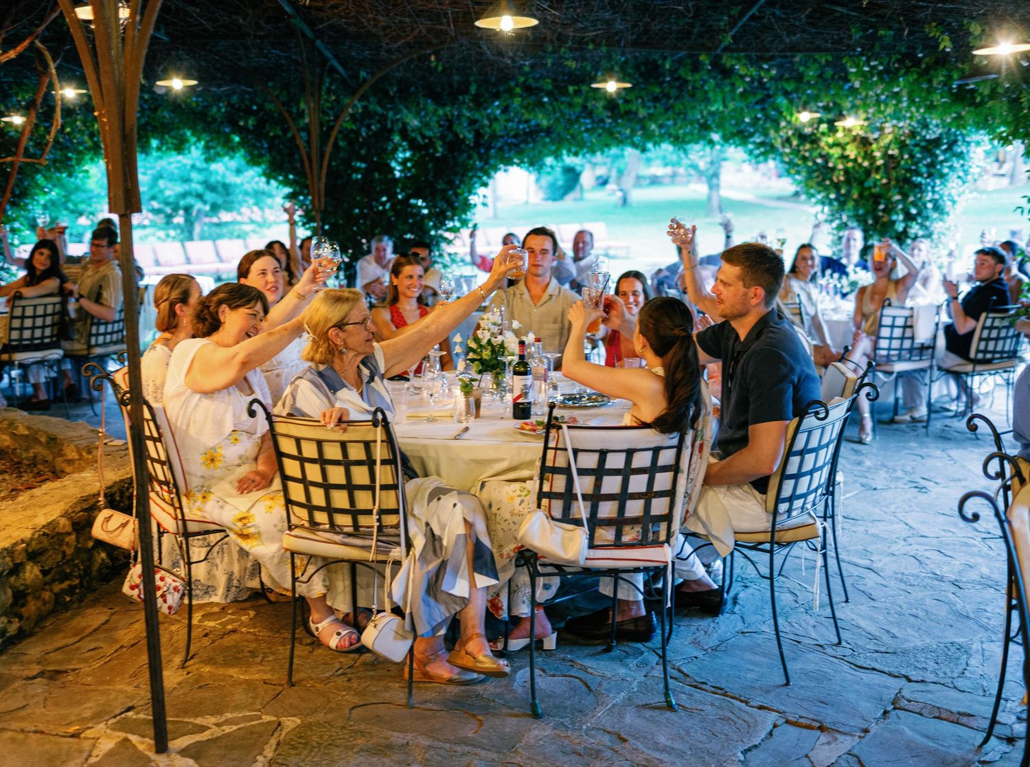 People gathered at tables for an outdoor evening dining event under string lights and trees.