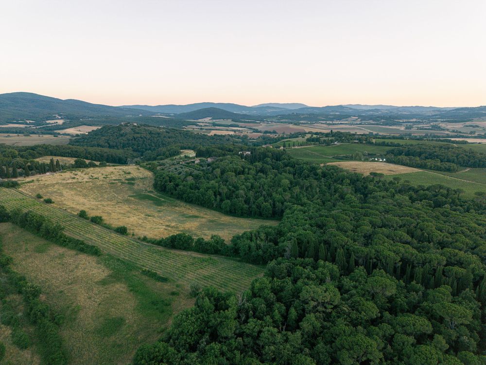 Rolling hills and Tuscan countryside stretch across a scenic rural landscape under a bright sky.