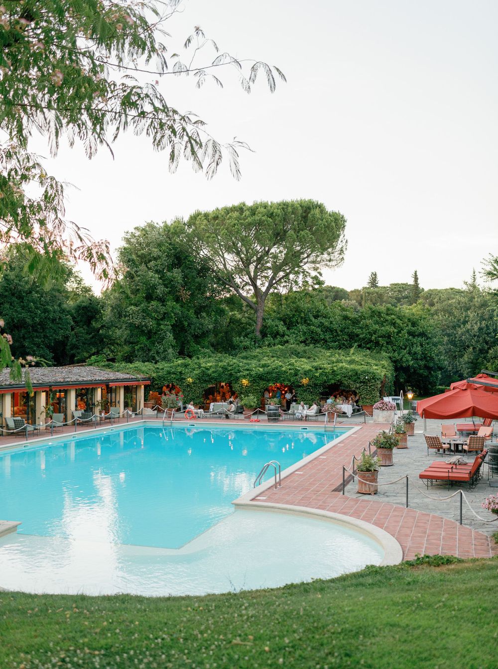 A luxury poolside resort setting with lounge chairs, covered pavilion, and landscaped grounds during golden hour at Borgo San Luigi.