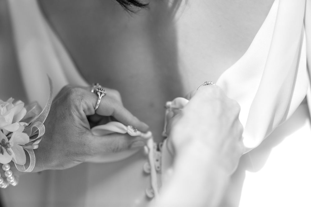 A close-up black and white photograph shows several bridal gowns hanging on a rack in a dress shop.