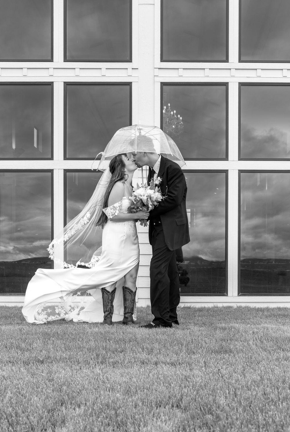 Black and white panoramic wedding photograph showing couple sharing an intimate moment outdoors against a modern building.
