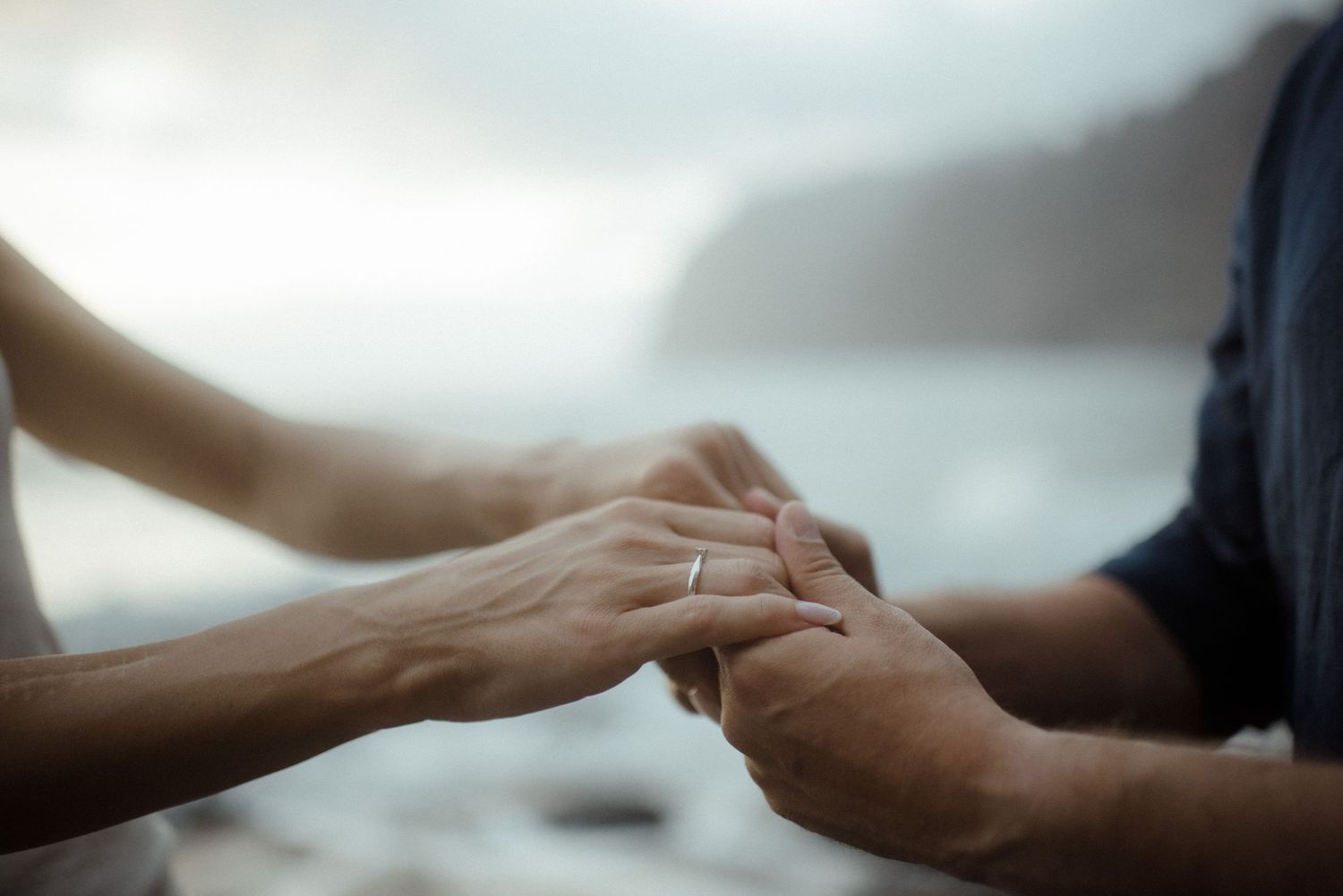 Two hands reach out to clasp together in support and unity against a soft, blurred background.