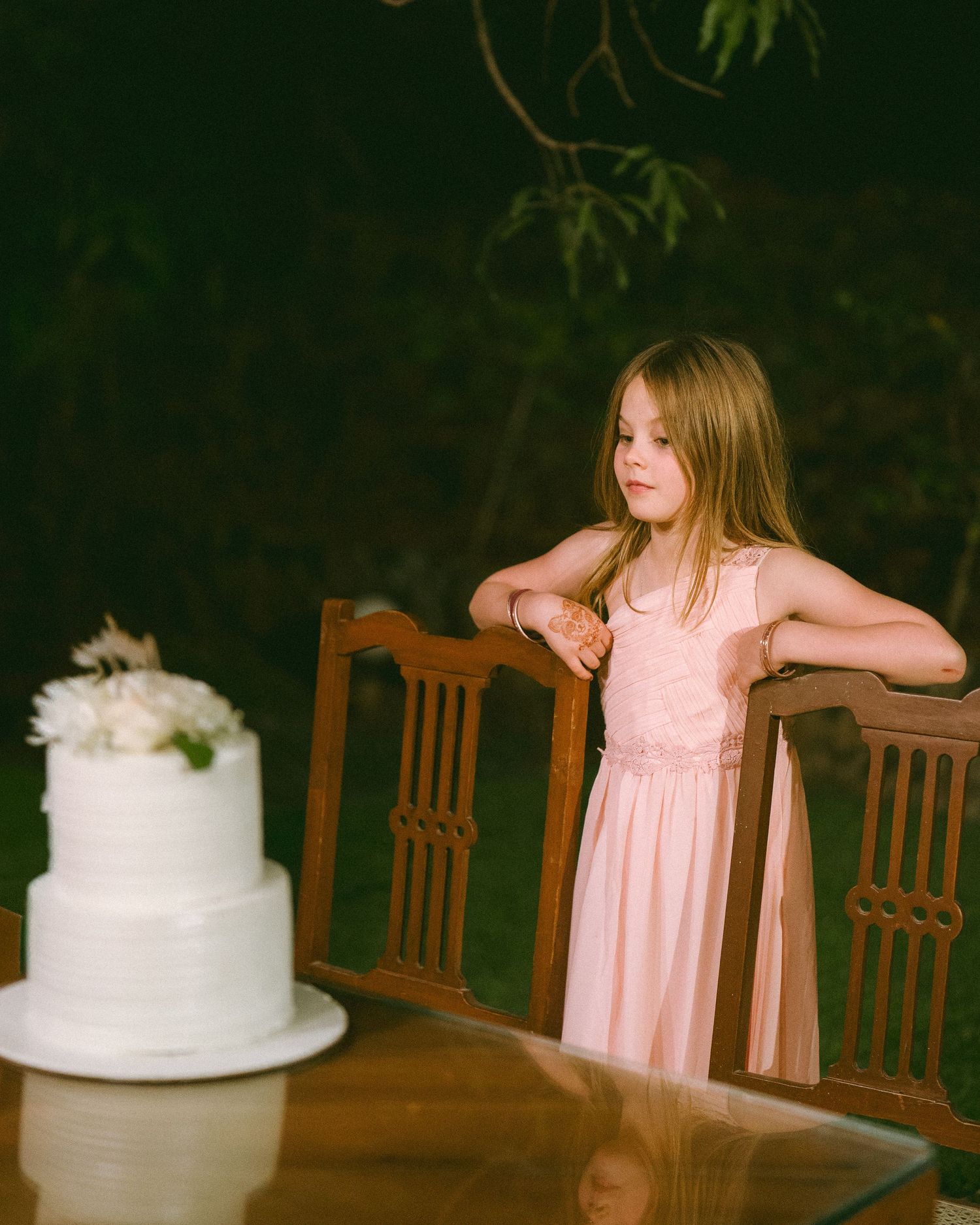 Young guest in pink dress posing near an elegant white wedding cake by the best wedding photographer in London & Birmingham.