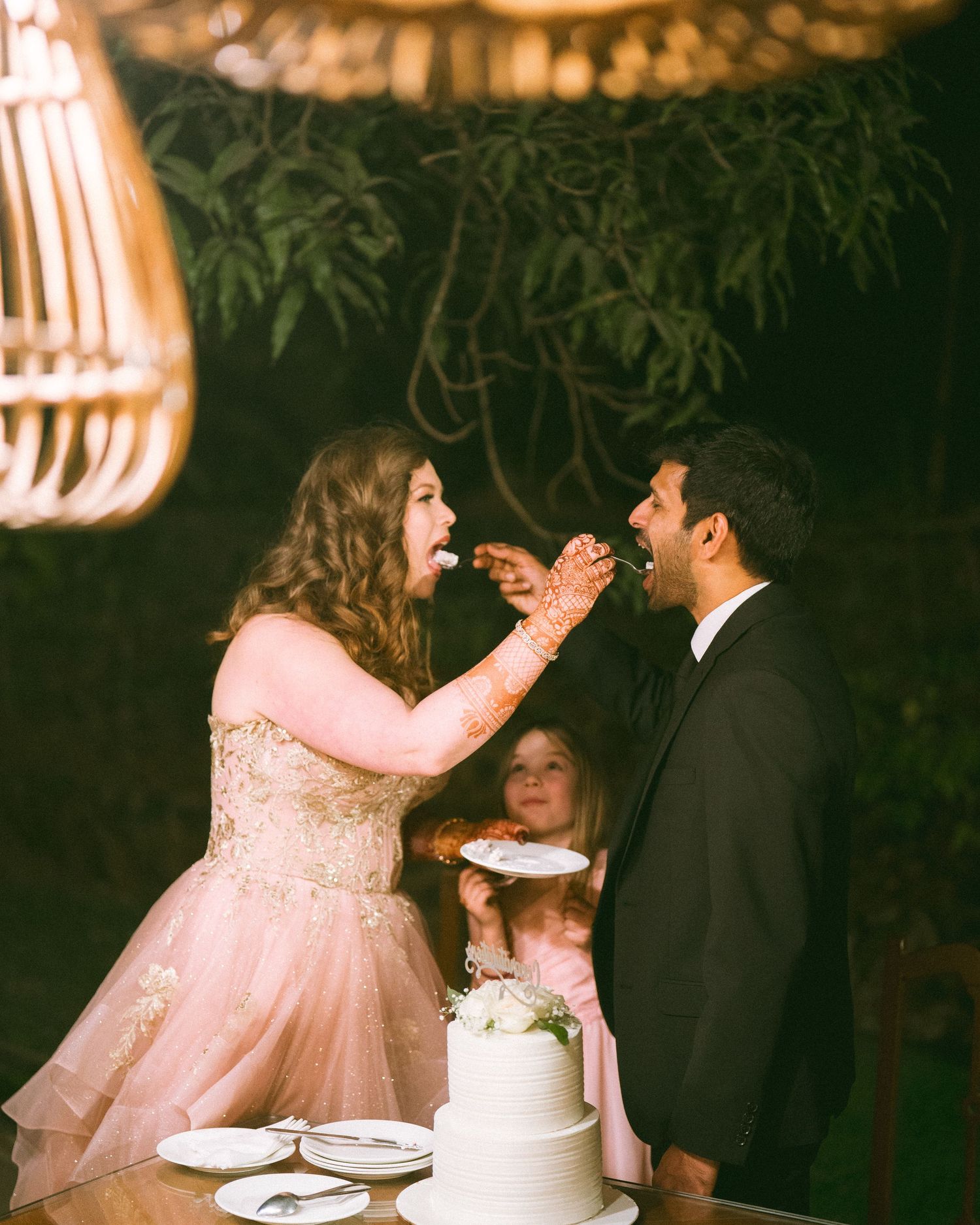Couple playfully feeding each other wedding cake at an evening celebration by the best wedding photographer in London & Birmingham