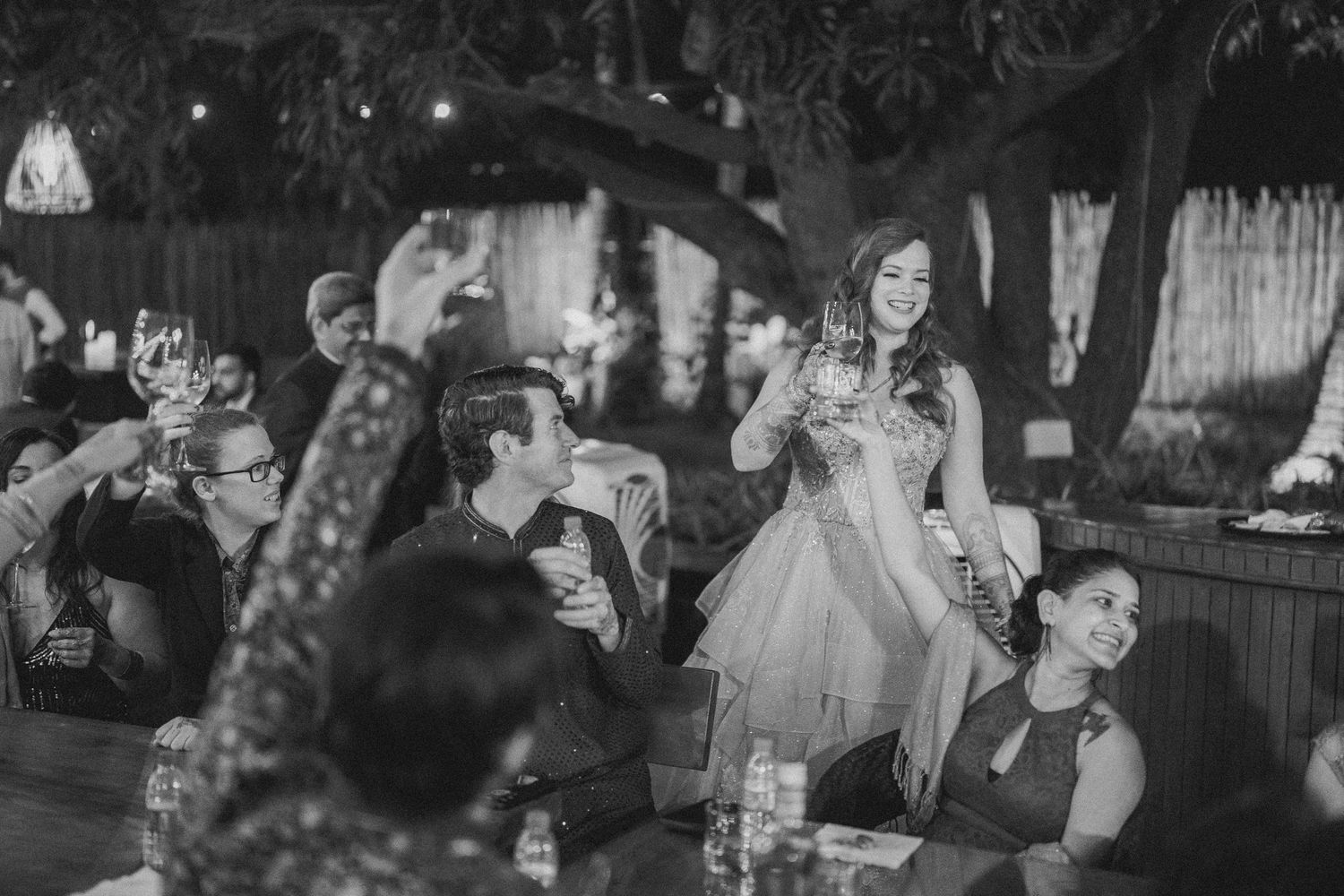 Thought processWedding reception crowd raising glasses in celebration under string lights by best wedding photographer in London