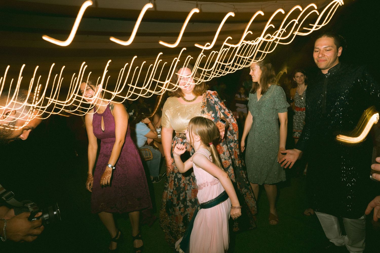Wedding guests dancing under decorative string lights with light trails in a dark venue by a wedding photographer in London