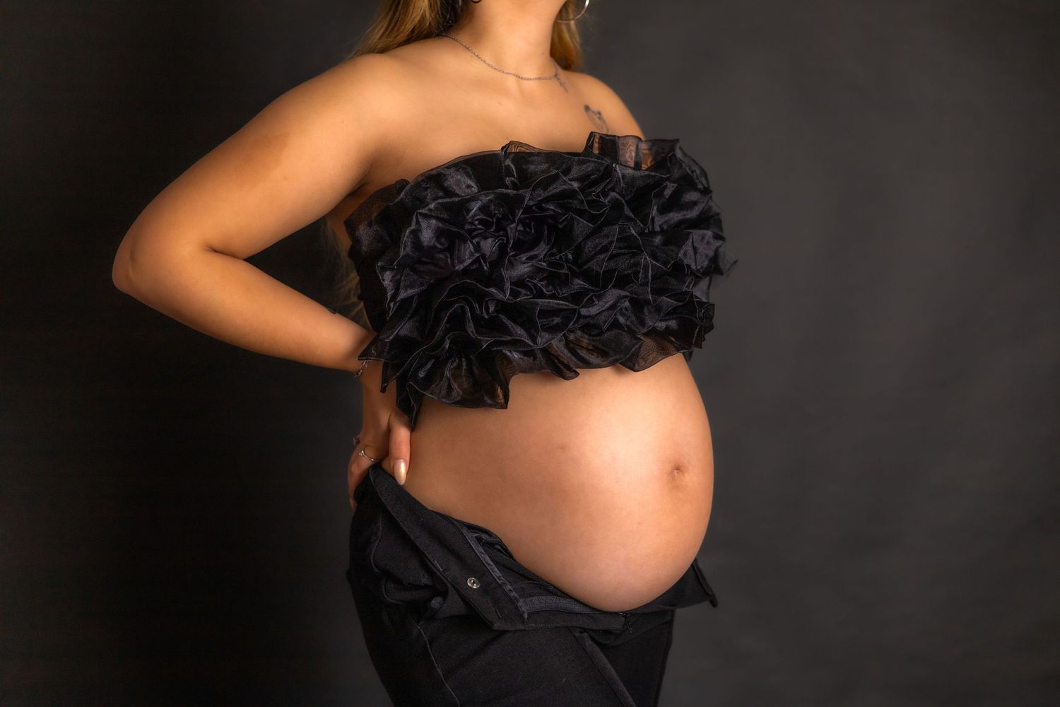 Artistic maternity photoshoot with black lace against dark background.