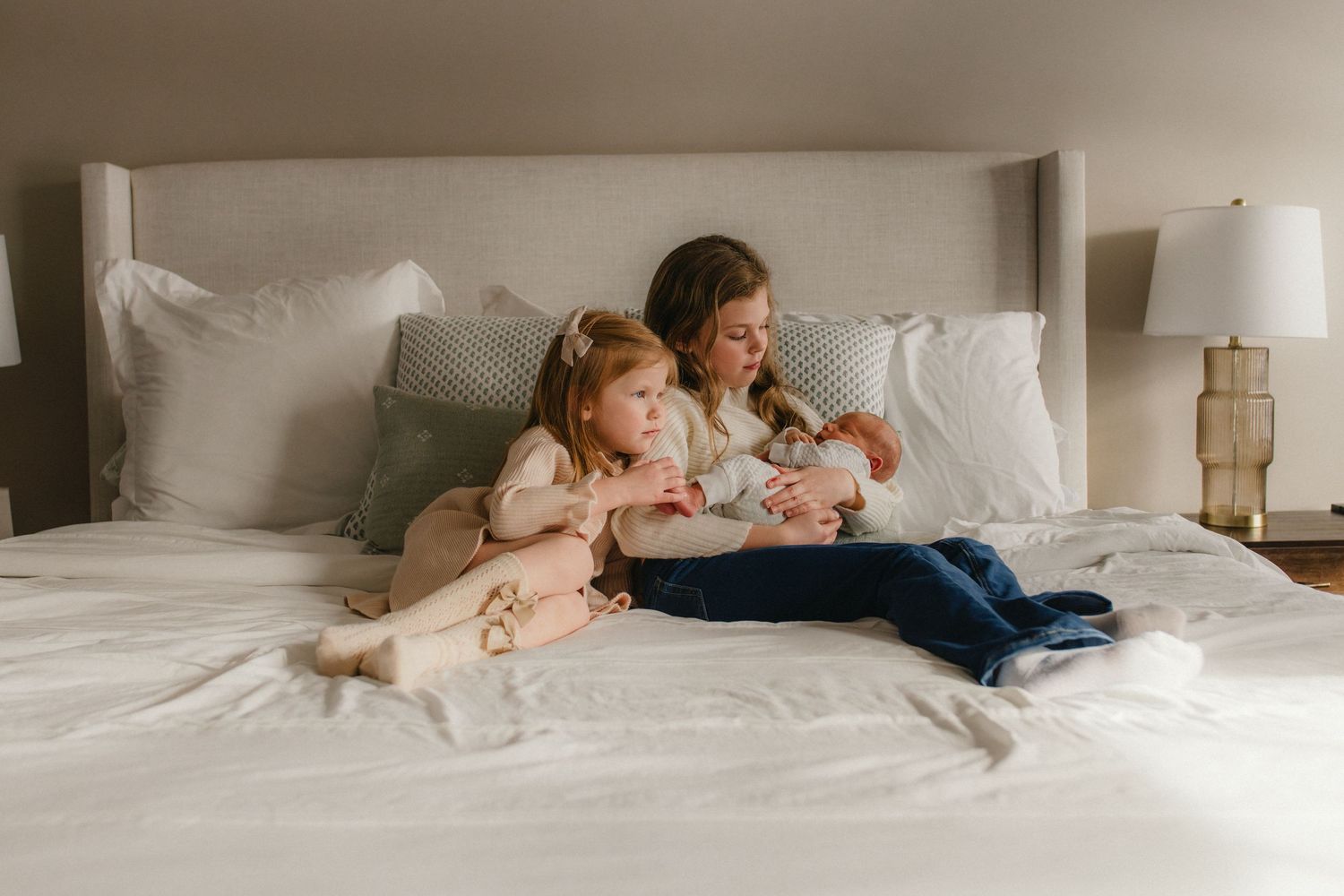 People relaxing together on a white bed in a cozy bedroom setting with soft lighting and neutral decor.