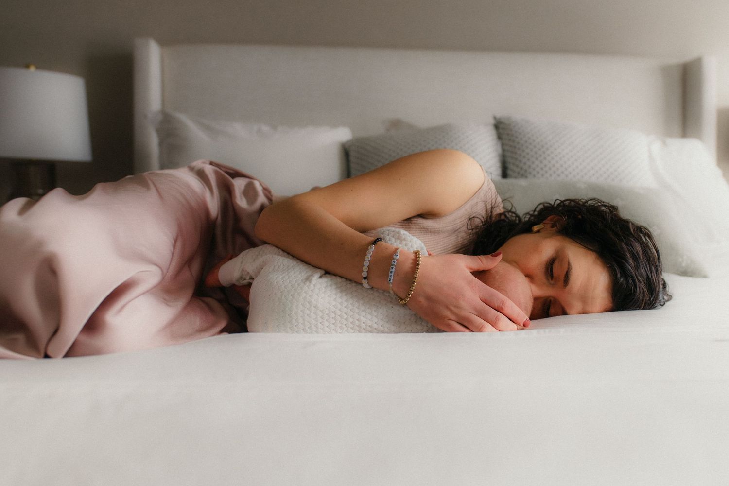 Someone peacefully sleeping in a white bed with pink bedding while curled up on their side.
