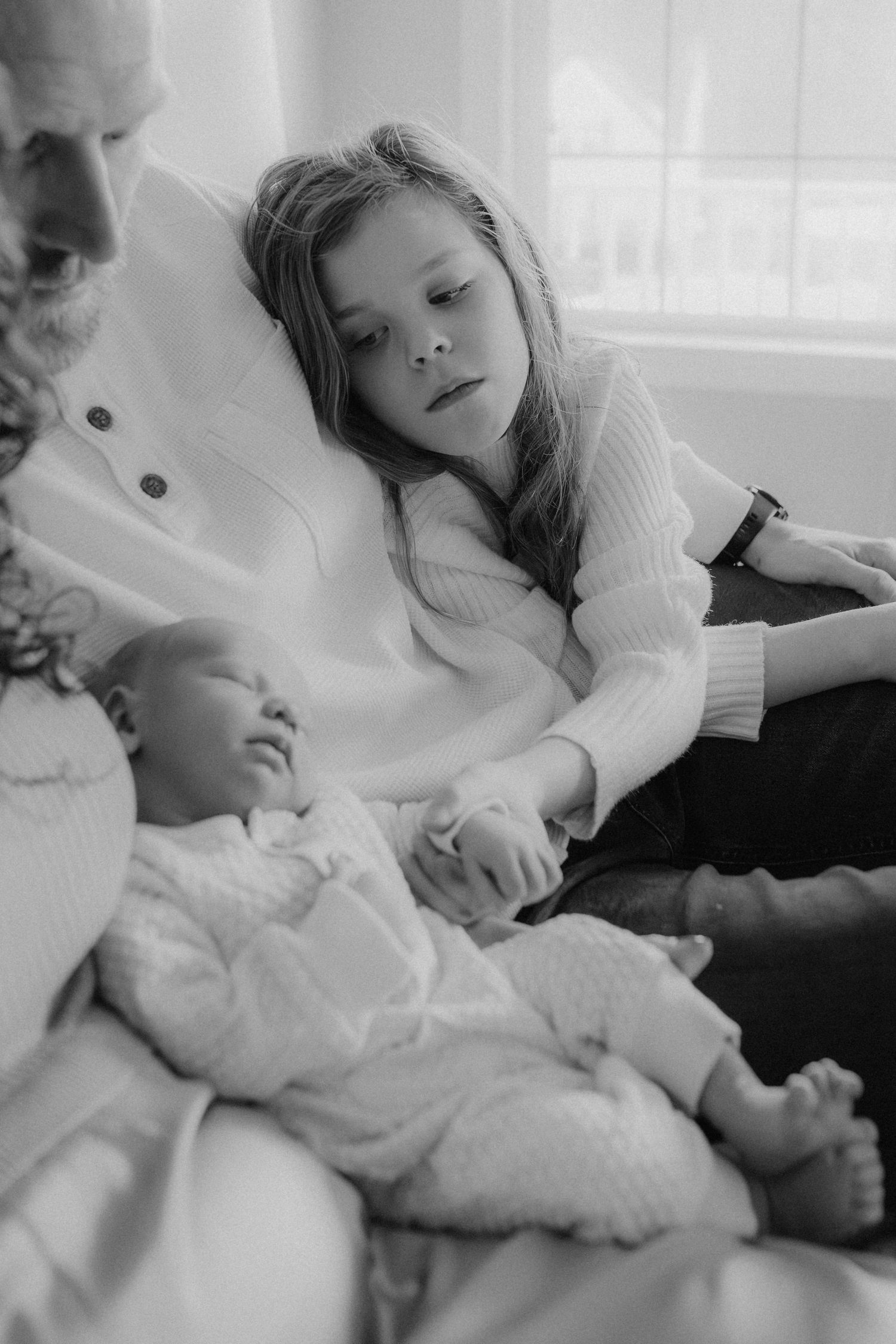 A tender black and white family moment showing people relaxing together with a sleeping baby in white clothing.