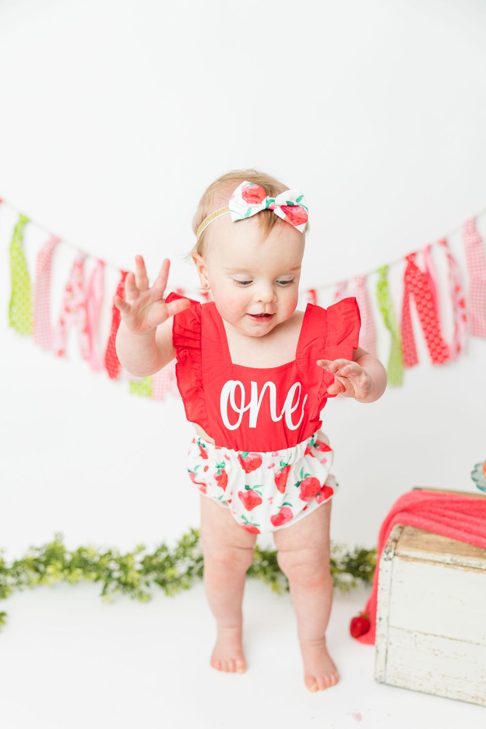 Colorful strawberry themed first birthday setup with pink and green fabric banner and white wooden crate props.