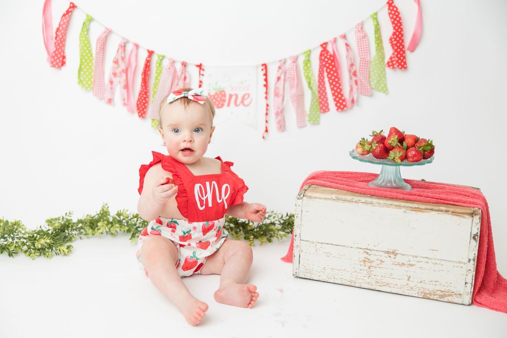 First birthday photo setup featuring strawberry themed decor, pink banner, and vintage white wooden crate.