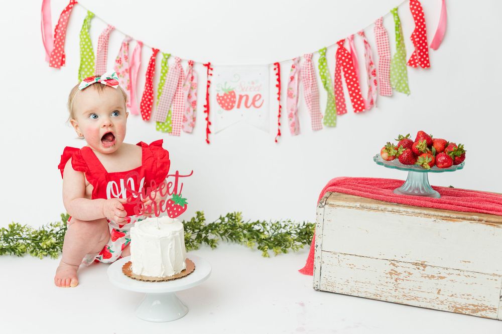 Festive birthday setup with white cake, strawberries, and pink and gold banner decorations against white backdrop.