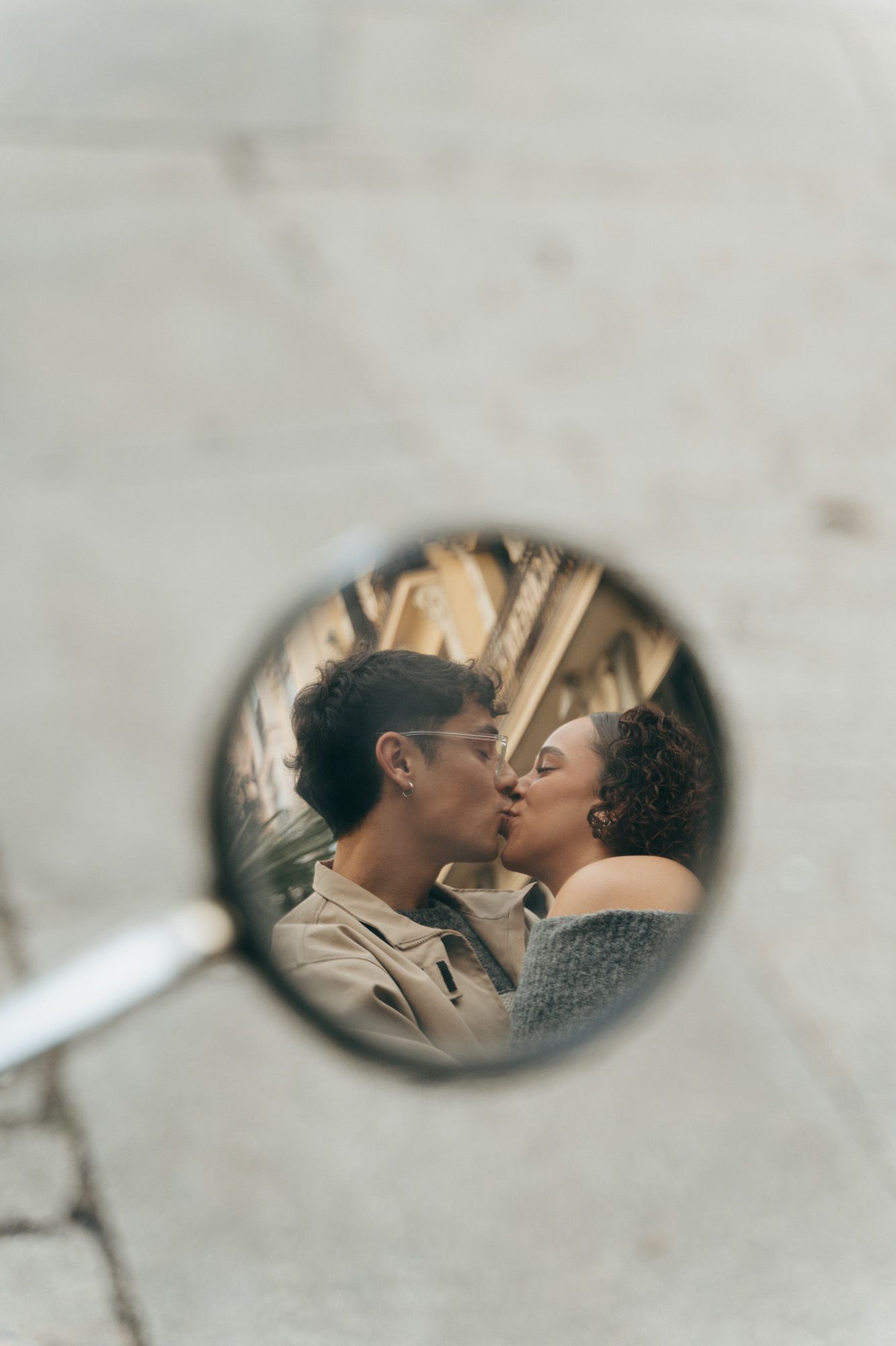 A tender romantic moment captured through a circular frame showing a couple sharing a gentle kiss.