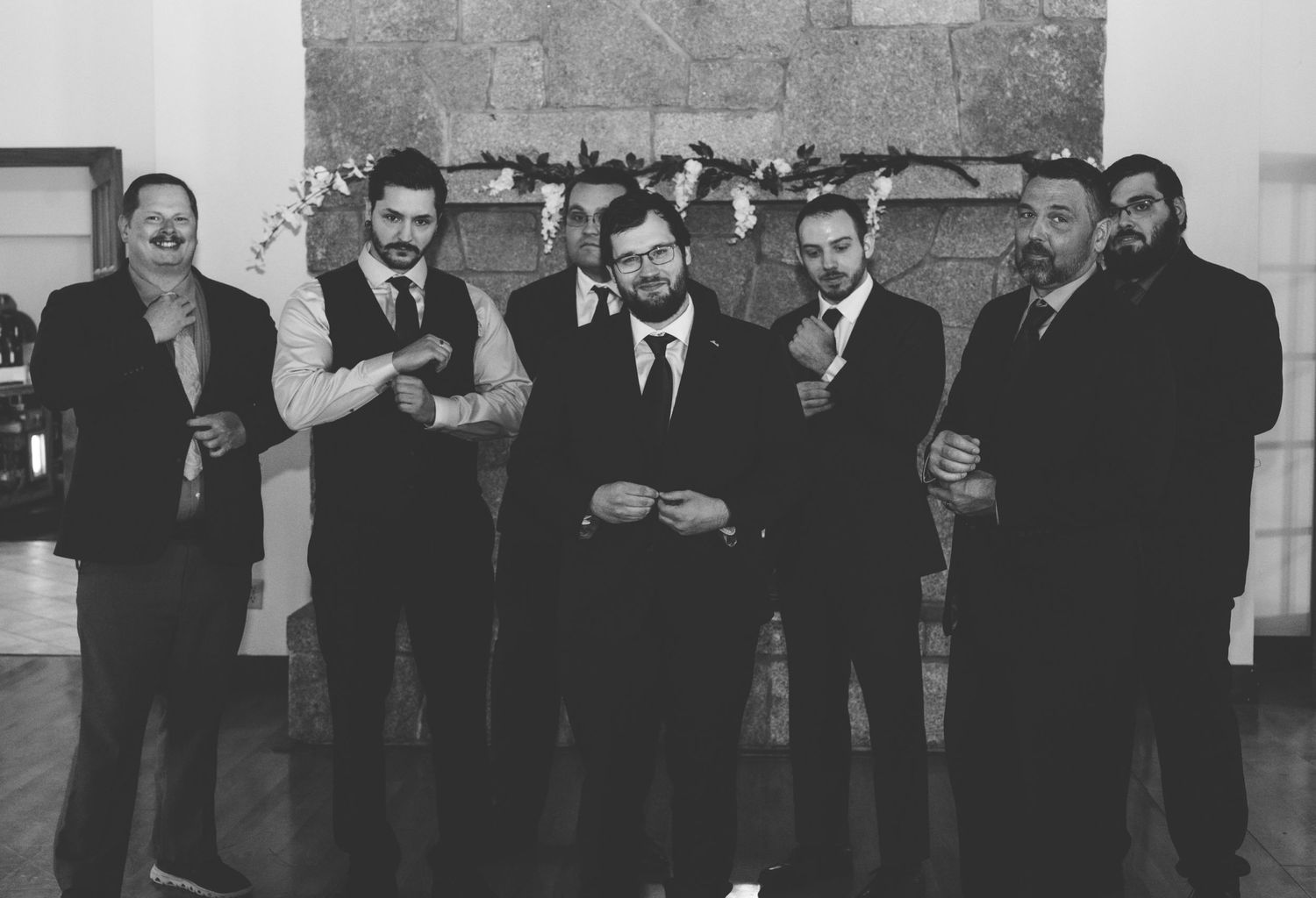 Black and white group photo of formally dressed people posing against a stone wall.