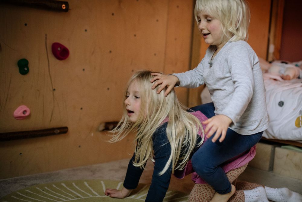 Two children play energetically together on a climbing wall, showing joyful movement and interaction.