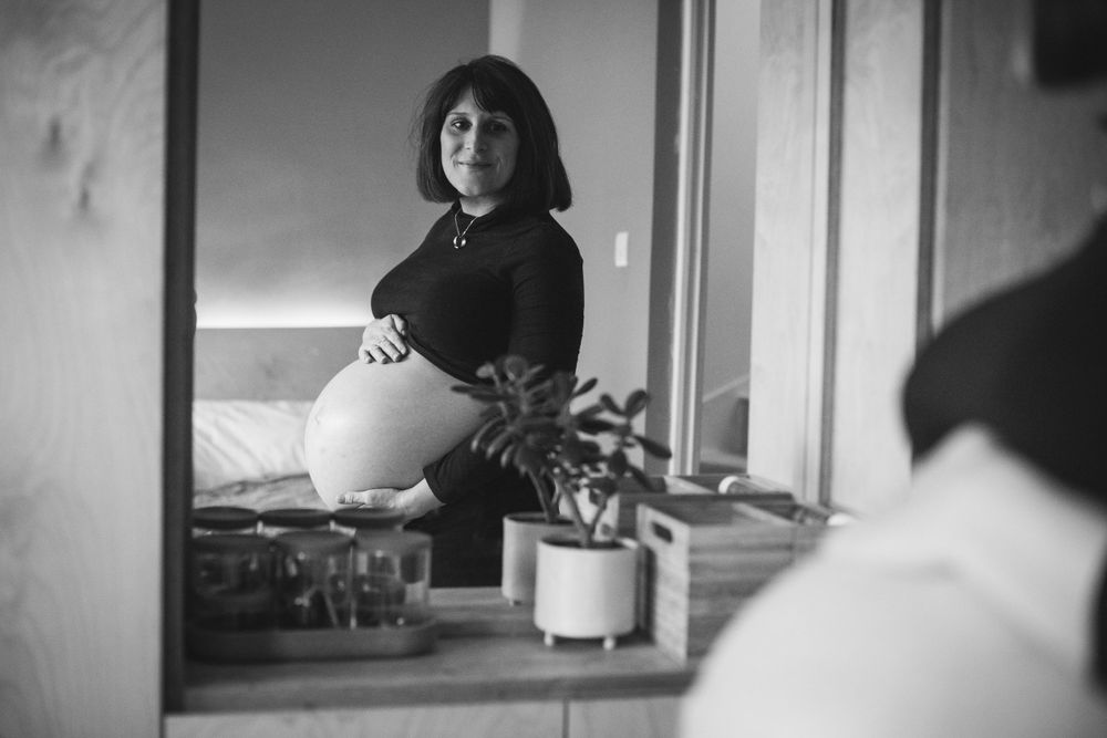 A person sits near a window while looking in a mirror, creating a reflective black and white composition.